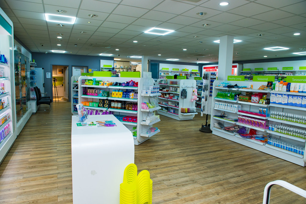 Community pharmacy retail floor with illuminated wall shelving and a consultation counter