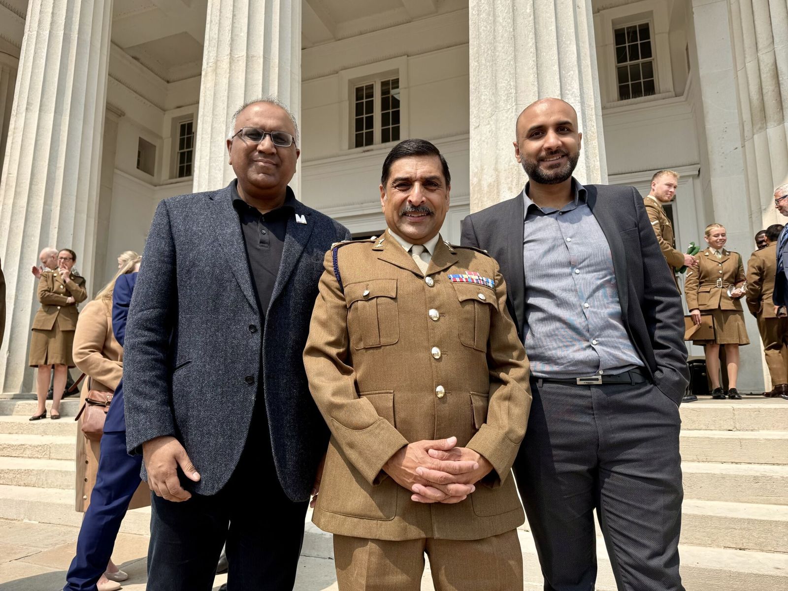 Safaraz Ali MBE with colleagues and a military officer outside a historic building