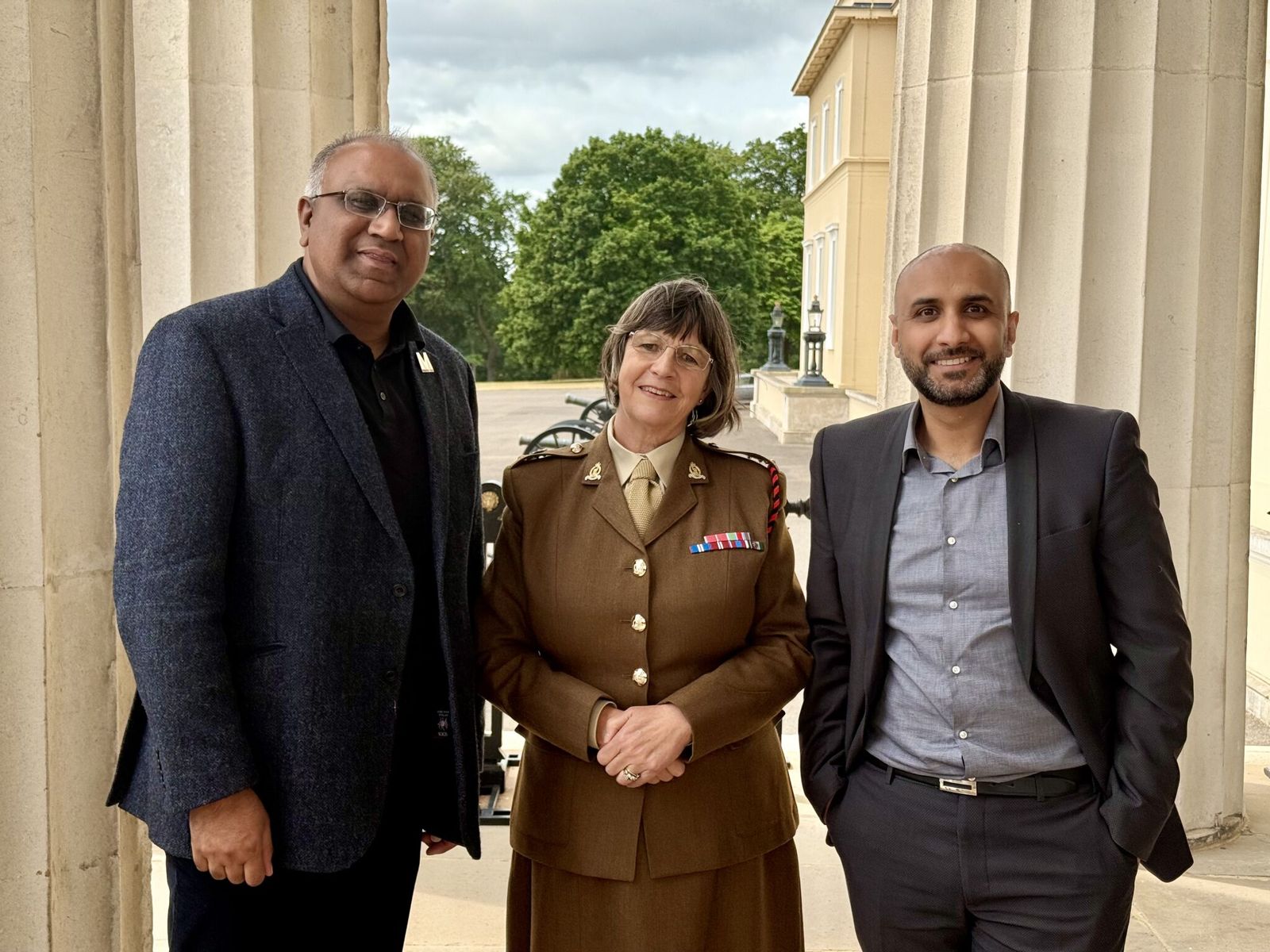 Safaraz Ali MBE with colleagues and a military officer outside a historic building