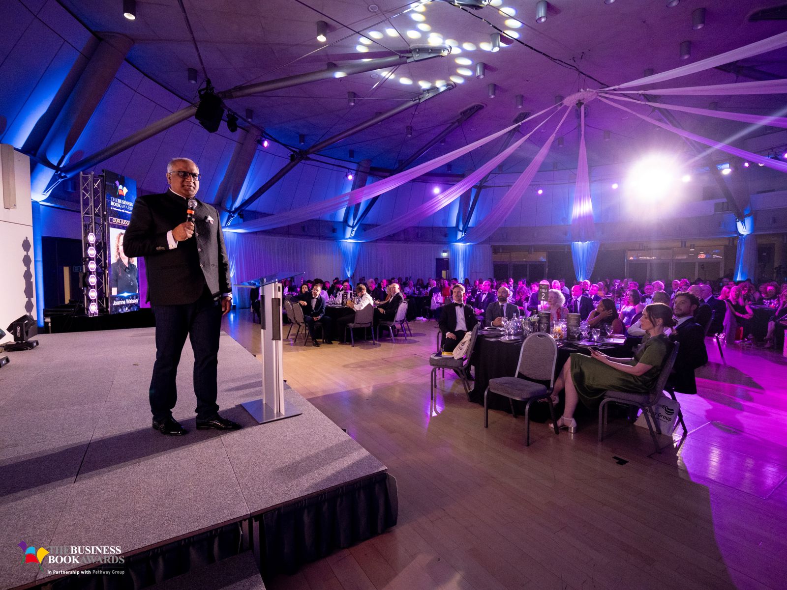 Safaraz Ali MBE speaking to a large audience at an awards event