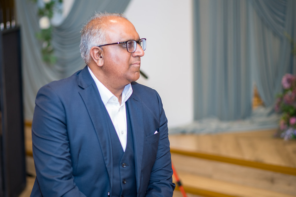 Safaraz Ali MBE listening attentively at a business event, wearing a navy suit and glasses
