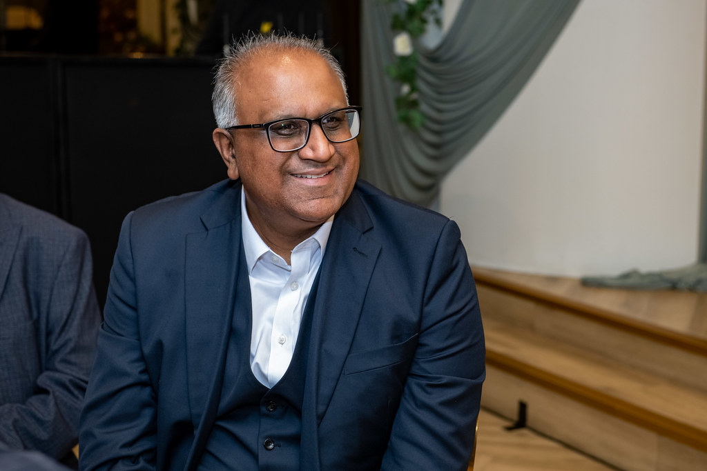 Safaraz Ali MBE smiling in conversation with others at a business gathering